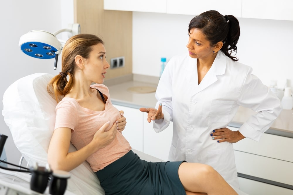 Experienced plastic surgeon consulting a woman at a clinic about natural breast augmentation, discussing options like fat transfer for subtle and proportionate enhancement.
