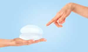 Close-up of a woman's hand pointing at breast implants against a blue background, representing options for breast augmentation procedures.