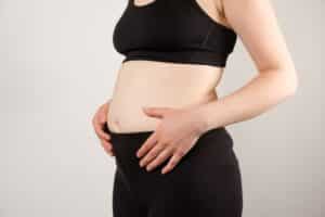 A woman displays a bloated belly after pregnancy, highlighting excess weight concerns and considering breast augmentation as part of her body restoration goals