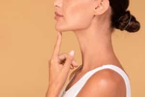 Side view of young woman touching face after chin augmentation, showing satisfaction with plastic surgery results