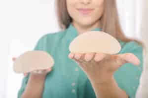 Woman holding breast implant during consultation for revision surgery and implant evaluation
